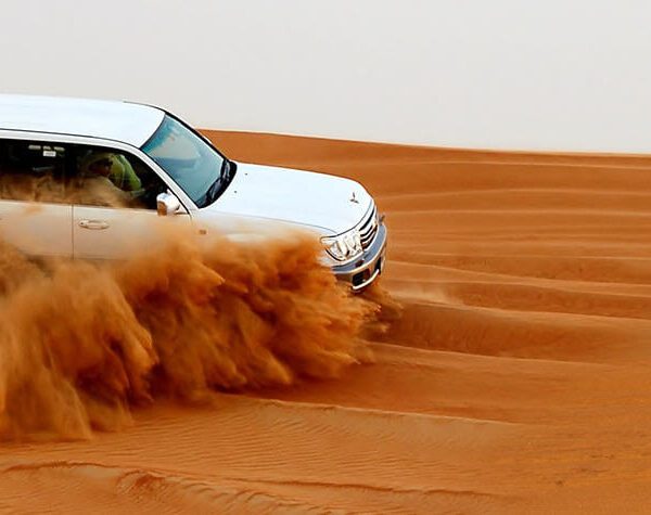 Sunrise Desert Safari Dubai A dynamic shot of a white SUV accelerating across a desert dune, creating a cloud of sand, illustrating a desert safari experience.